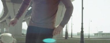 Profesyonel futbolcunun şehir köprüsünün altında spor giyim hokkabazlığı topunun anamorfik görüntüsünü yukarı kaldır.