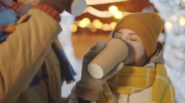 Genç aşıklar kahve içmek için bardaklarını yudumlarken, öpüşürken ve kucaklaşırken sokakta Noel ışıklarıyla süslenmiş romantik bir randevu geçiriyorlar.