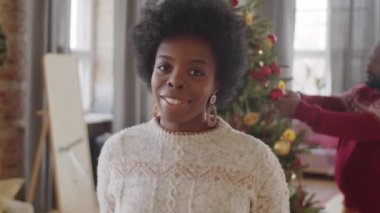 Kocası arka planda Noel ağacını süslerken Afro-Amerikan güzel bir kadının fotoğrafına bakıp gülümsüyor.