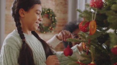 Neşeli Afro-Amerikan anne ve kızı evde Noel ağacını birlikte süslüyor ve konuşuyorlar.