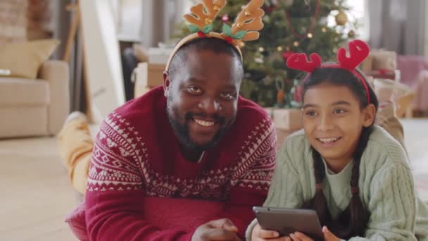 크리스마스 머리띠에 디지탈 태블릿 바닥에 웃으며 카메라에 포즈를 취하는 미국인 — 비디오