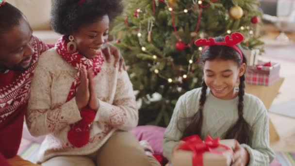 ハッピーアフリカ系アメリカ人の女の子は ギフトボックスや巨大な両親からクマのおもちゃを取りながら 自宅でクリスマスプレゼントを共有 — ストック動画