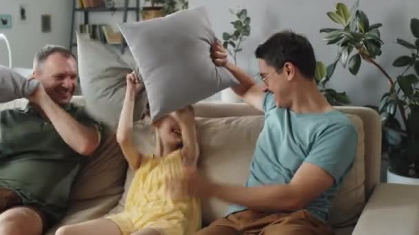 在客厅里 一对快乐的同性恋夫妇和他们可爱的女儿在打斗枕头 拍了一张水平的中景照片 — 图库视频影像