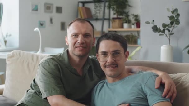 中近景ポルノのショットビデオのハンサムな成熟したゲイの男性の愛で一緒に座っています上のソファの上にリビングルームでカメラを見て — ストック動画
