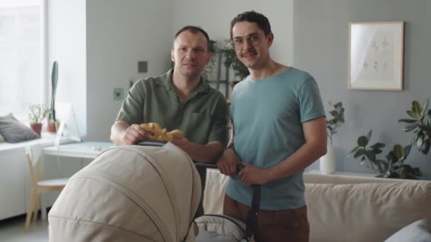 結婚したゲイのカップルの肖像画過ごす時間で自宅でリビングルームとともに彼らの認識できない新生児でPram笑顔でカメラ — ストック動画
