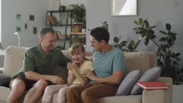 有趣的已婚同性恋夫妇和他们可爱的女儿坐在客厅的沙发上互相爱抚 动作缓慢 — 图库视频影像