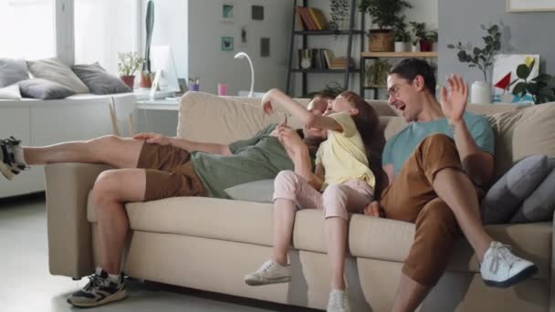 与女儿一起在电视上看滑稽电影的现代同性恋夫妇在家里度过的广泛镜头 — 图库视频影像
