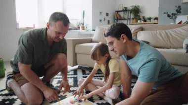 Küçük kızıyla birlikte oturma odasında oturmuş parmak boyası yapan eşcinsel bir çiftin el kamerasıyla çekilmiş yüksek açılı görüntüleri.