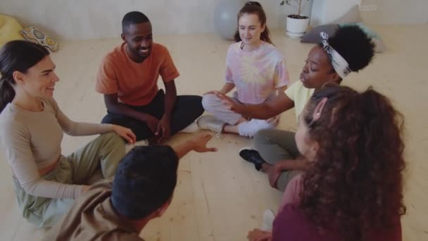 スタジオの床に座って手をつなぎ笑顔でスポーツウェアの若い多民族のダンサーのグループ — ストック動画