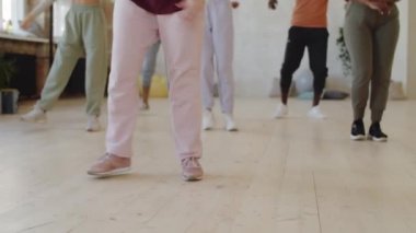 Alçak kesim, spor giyim kuşamında bir grup çoklu etnik öğrencinin dans kursunda kollarını sağa sola hareket ettirmelerini gösteriyor.