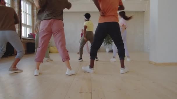 スタジオでクラスを与えながら 若い多民族の人々のグループにダンスの動きを示す楽しい女性トレーナーのショットでズーム — ストック動画