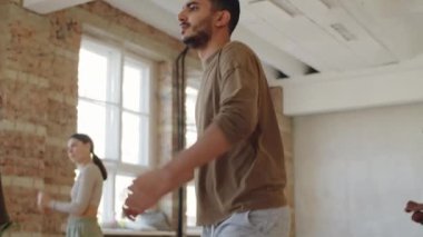 Dans kursunda bir grup çoklu etnik grupla birlikte gülümseyen ve dans eden neşeli orta doğulu adamı kaldır.