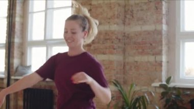 Spor giyim bölümünde genç sarışın bir dansçı stüdyoda enerjik bir dans sergiliyor.