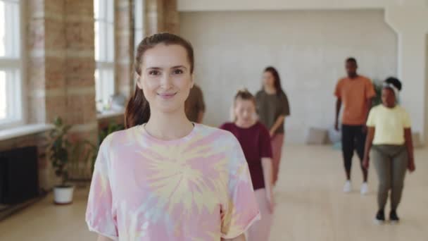 ダンスのクラスに立つ若い白人女性の肖像画 笑顔とバックグラウンドでグループトレーニングとしてカメラのためにポーズ — ストック動画