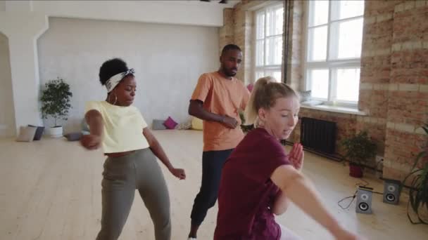スタジオでプライベートダンスのレッスンを受けながら 若いアフリカ系アメリカ人のカップルが白人女性教師と一緒にダンスのショットを下に傾ける — ストック動画