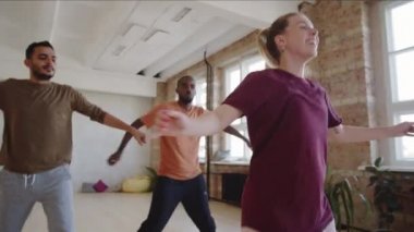 Genç Afro-Amerikalı ve ortadoğulu erkekler spor giyim sektöründe beyaz kadın öğretmenle dans ederken stüdyoda ders alıyorlar.