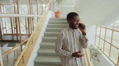 Modern binada merdivenlerde duran ve cep telefonuyla konuşan yakışıklı Afro-Amerikalı adam.