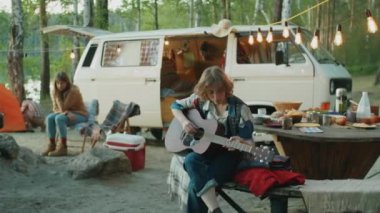 Ormanda arkadaşlarıyla kamp yerinde otururken gitar çalan genç bir kadının arkası.