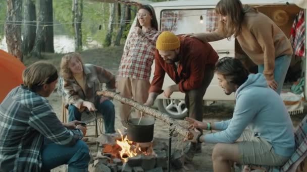 Young Man Stirring Food Cooking Pot Campfire Chatting Cheerful Friends — Stock Video
