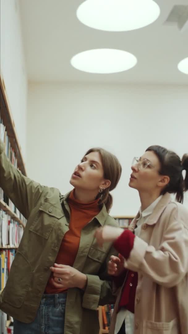 Scatto Verticale Due Giovani Donne Che Prendono Libro Dallo Scaffale — Video Stock
