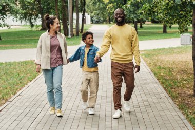 Üç kişilik aile parkta yürüyor.