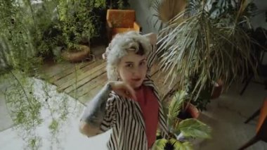 Dövmeli kolları olan genç bir kızın bir sürü yeşil bitkiyle dans ettiği bir oda.