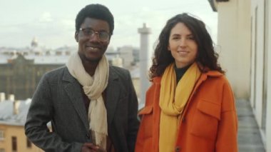 Pozitif Afro-Amerikalı erkek ve beyaz kadının portresi şehrin çatı terasında yan yana duruyor, kameraya bakıyor ve gülümsüyor.