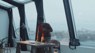 Genç Afro-Amerikalı iş adamı dizüstü bilgisayarı kapatıyor, masa lambasını kapatıyor, ceketini ve çantasını alıyor ve iş gününden sonra ofisinden ayrılıyor.