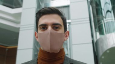 Düşük açılı göğüs yukarı. Korunaklı yüz maskesi takmış beyaz iş adamı Coronavirus salgını sırasında kameraya poz verirken görülüyor.