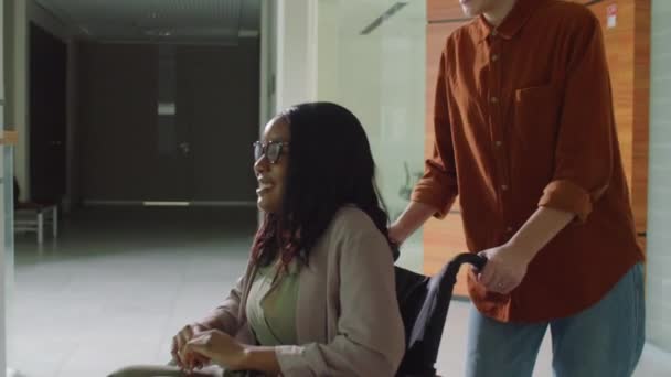 Alegre Mujer Caucásica Empujando Colega Afroamericano Silla Ruedas Centro Oficinas — Vídeos de Stock