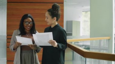 Afro-Amerikalı iş kadını, ofiste birlikte çalışırken melez bir kadın meslektaşla belgeleri tartışıyor.