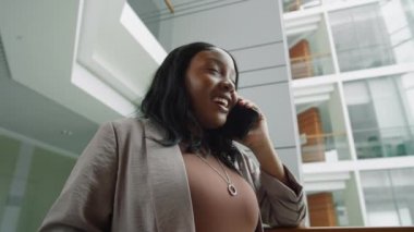 Afro-Amerikalı iş kadınının ofis merkezinde cep telefonuyla konuşurken düşük açılı görüntüsü.