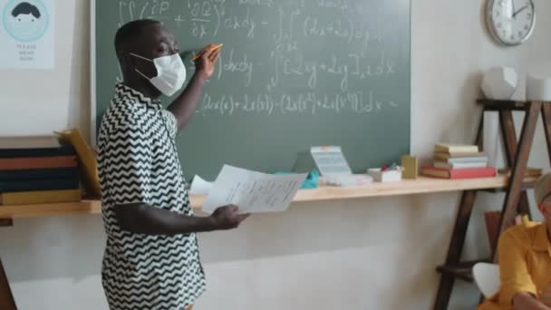 戴防护面罩的美国黑人大学生拿着试卷 指着黑板上的数学公式 在科维德19流感大流行期间边上课边说话 — 图库视频影像