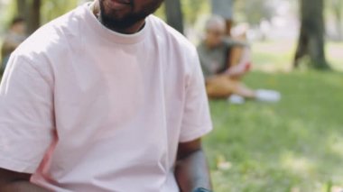 Genç Afro-Amerikan erkek öğrencinin yaz günü dışarıda ders çalışırken parkta oturup dizüstü bilgisayarda yazışmasını çek.