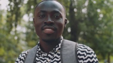 Yaz günü sırt çantasıyla dışarıda kameraya bakıp gülümseyen Afro-Amerikan erkek öğrencinin portresi.