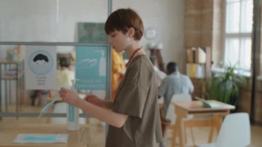Çok ırklı lise öğrencileri tek kullanımlık yüz maskeleri takıyor, el dezenfektanı uyguluyor ve dersten önce sınıflarında masalarına yürüyorlar.