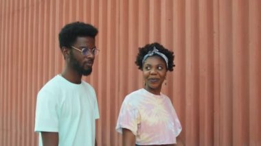 Genç Afro-Amerikalı erkek ve kadın yaz günü birlikte yürüyorlar, gülümsüyorlar ve sohbet ediyorlar.