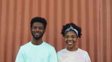 Genç Afro-Amerikan erkek ve kadın portresi. Kameraya bakıyor ve gülümsüyor. Yaz günü şehir duvarına karşı poz verirken.