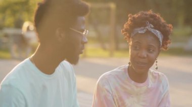 Genç Afro-Amerikalı kadın ve erkek güneşli bir yaz gününde parkta otururken konuşuyor.