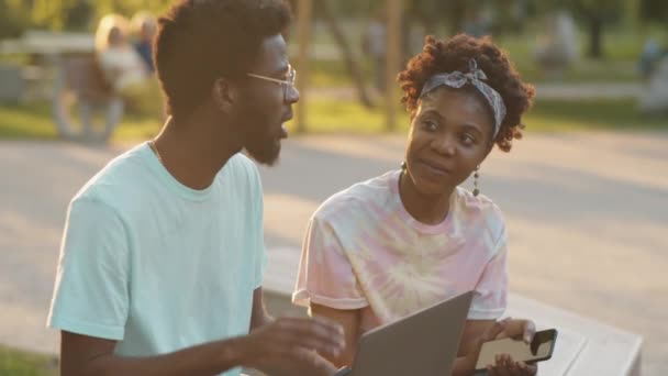Junge Afroamerikaner Sitzen Mit Laptop Und Smartphone Auf Parkbank Und — Stockvideo
