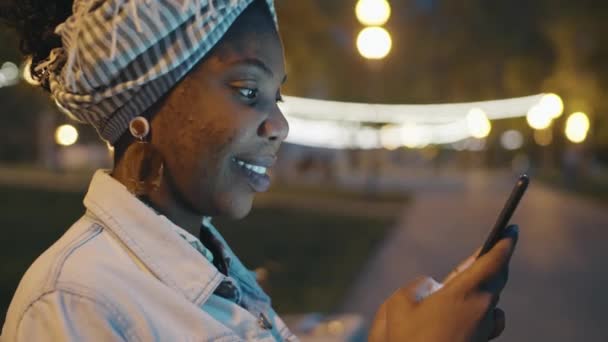 Neşeli Afro Amerikalı Kadın Akşamları Parkta Oturuyor Akıllı Telefondan Mesajlaşıyor — Stok video
