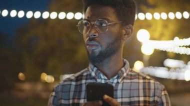 Gözlüklü genç Afro-Amerikalının akşamları park yerinde cep telefonu kullanırken ki görüntüsü.