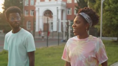 Genç Afro-Amerikalı kadın ve erkek yazın parkta birlikte yürürken gülümsüyor ve sohbet ediyorlar.