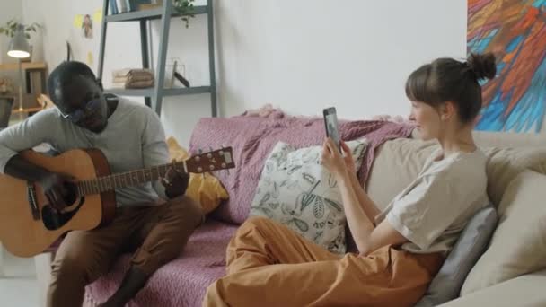 Joven Hombre Afroamericano Sentado Sofá Casa Tocando Guitarra Mientras Esposa — Vídeo de stock