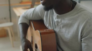Gitar çalan ve evde şarkı söyleyen Afro-Amerikalı genç adamın görüntüsünü kaldır.