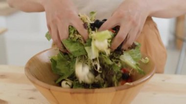 Ahşap kasede sebze salatası karıştıran tanınmayan bir kadının ellerini yakın plan çek.