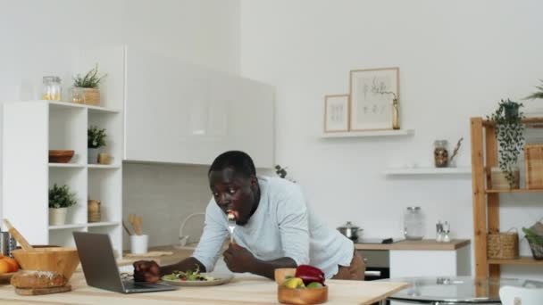 Joven Afroamericano Apoyado Mesa Cocina Comiendo Ensalada Verduras Usando Portátil — Vídeo de stock