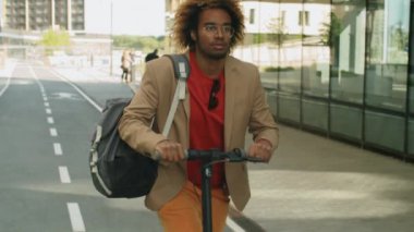 Genç Afro-Amerikalı iş adamının, şehir merkezinde, elektrikli scooter sürerken, yavaş çekimde...