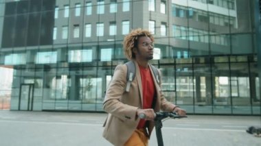 Sırt çantalı genç bir Afro-Amerikalı sabah işe giderken şehirde elektrikli scooter kullanıyor.