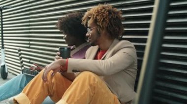 Genç Afro-Amerikalı kadın ve erkek, şehirde e-scooterlarla oturuyor, kahve içmek için içiyor, dizüstü bilgisayar kullanıyor ve konuşuyor.